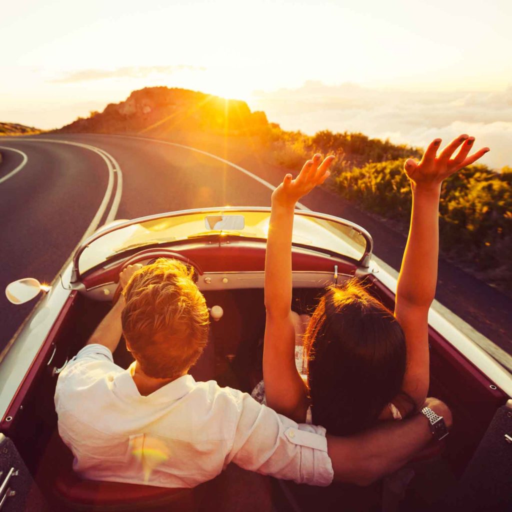 Couple in convertible driving at sunset after achieving business succession freedom