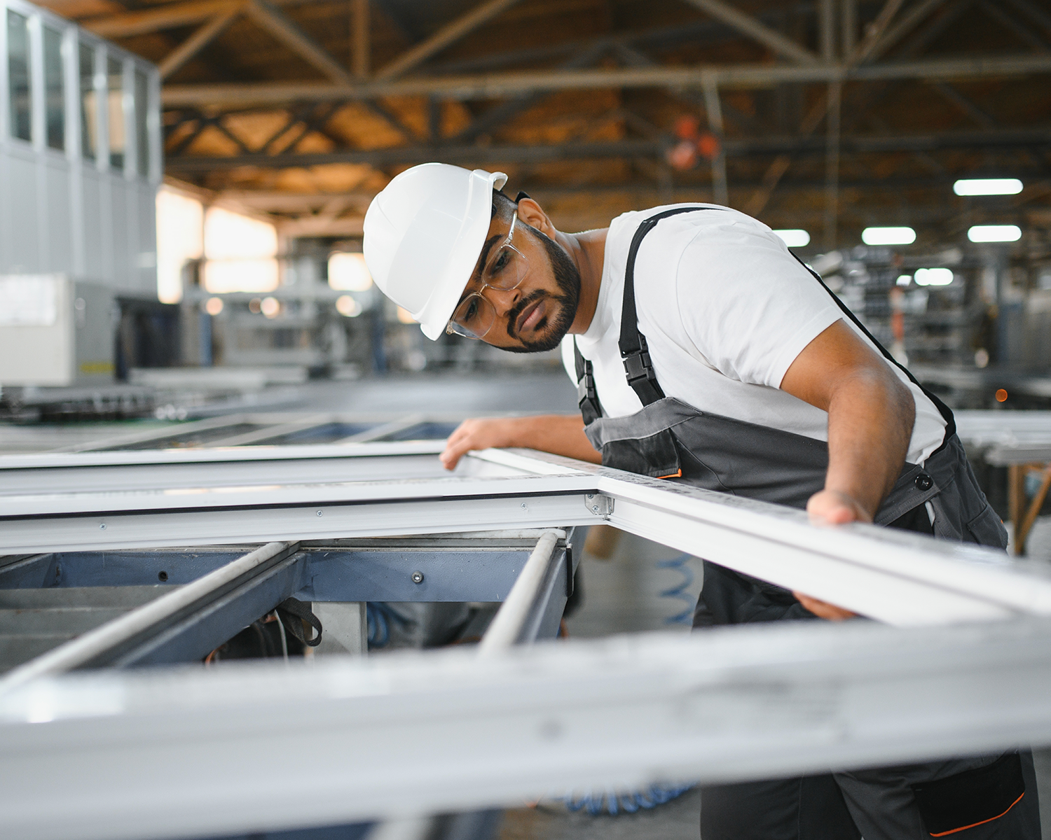 A worker in a hard hat and safety glasses inspects a high-end metal frame in an industrial factory setting, showcasing the precision of specialty manufacturing.