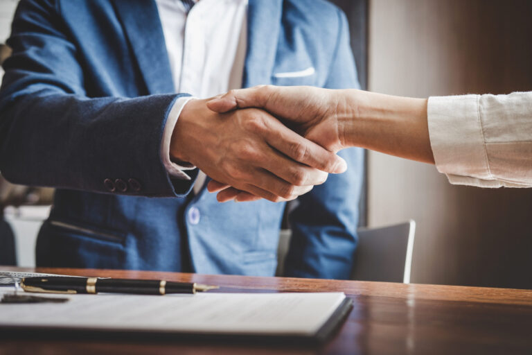 Two business people from an M&A Firm shaking hands over a desk, discussing the benefits of business transitions.