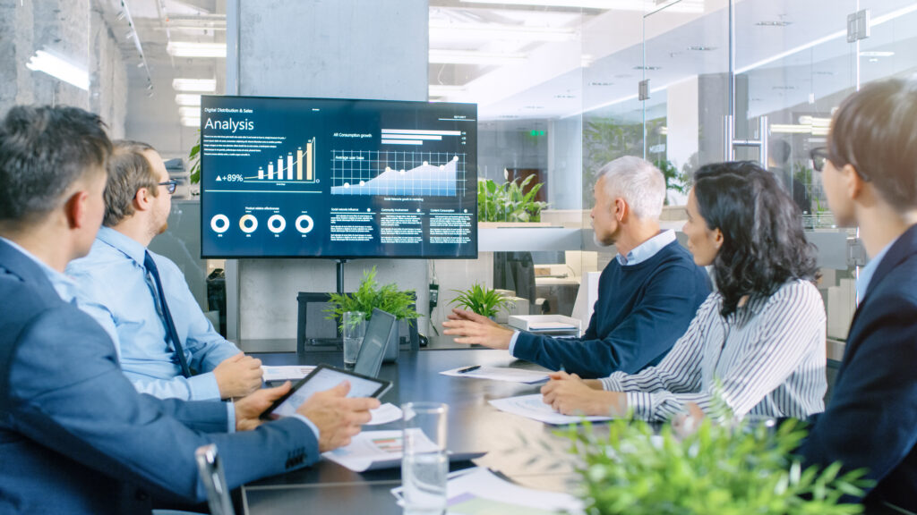 A group of investors sitting around a table looking at a CIM on a television.