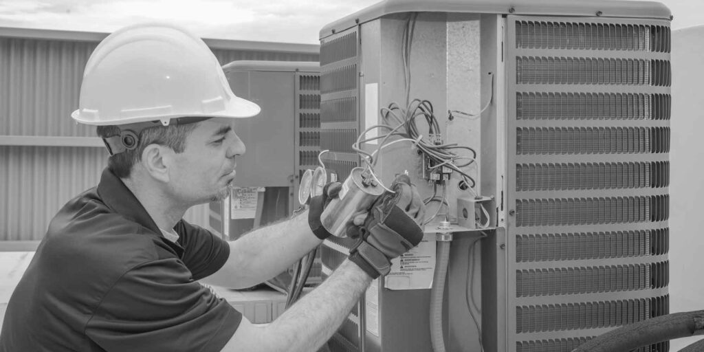 A technician in a hard hat and gloves works diligently on the wiring of an outdoor HVAC unit, showcasing the expertise of our HVAC business.