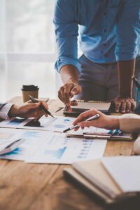 People at a table discussing the importance of business graphs and charts with pens, notebooks, and a coffee cup. They engage in lively conversation about the definition of Adjusted EBITDA and its significance to their company's financial health.