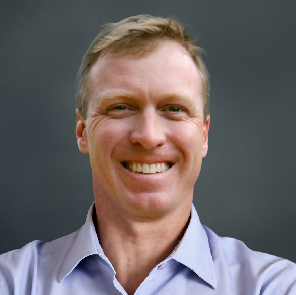 A person wearing a light blue shirt smiles in a headshot against a plain, dark background.