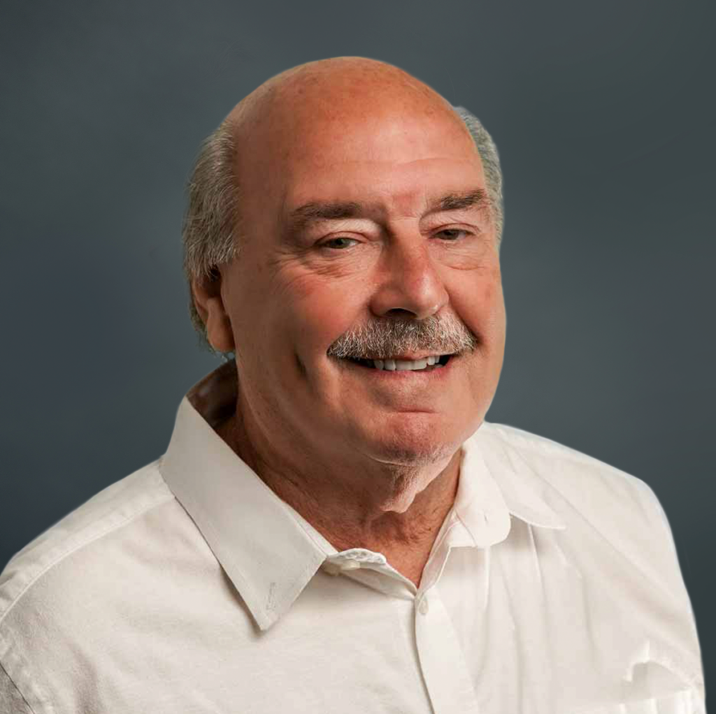 A man with a mustache wearing a white collared shirt against a gray background.