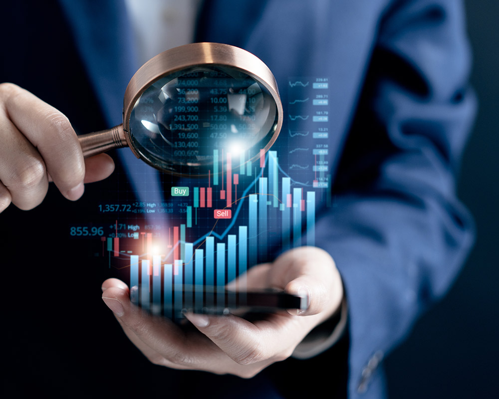 A person in a suit holds a magnifying glass over a smartphone displaying digital financial charts and trading indicators, highlighting the detailed analysis an M&A advisor brings to industry-specific transactions.