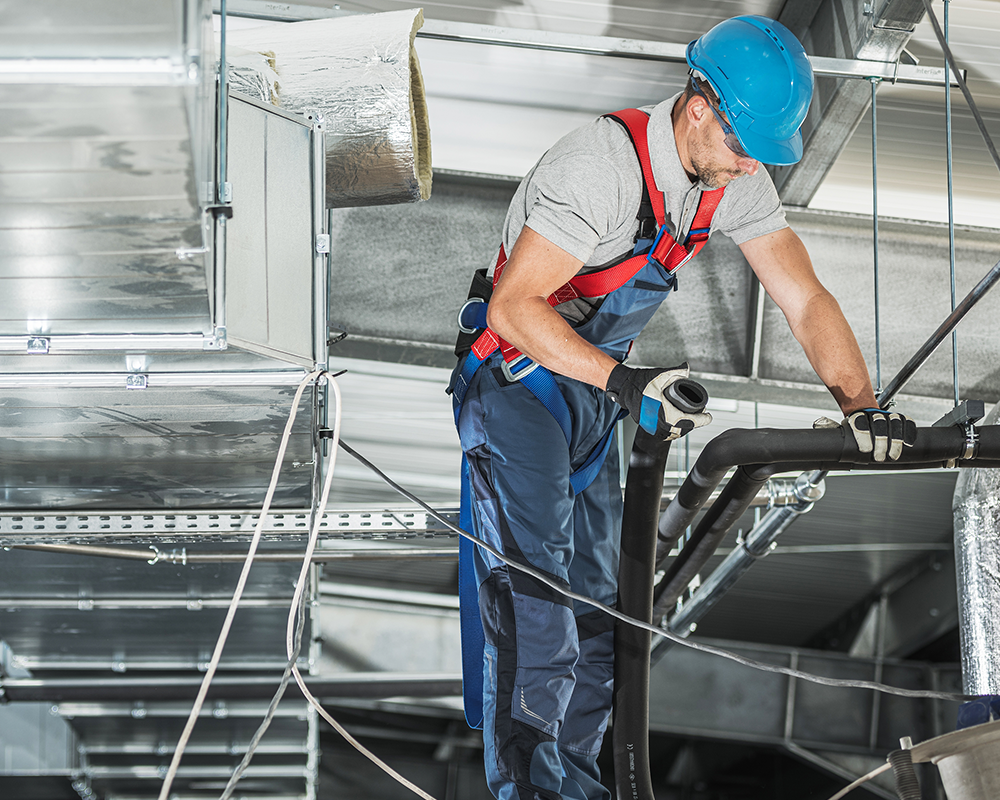 A worker wearing safety gear and a helmet installs or services HVAC ductwork on a ceiling, showcasing the expertise essential for a successful HVAC business.