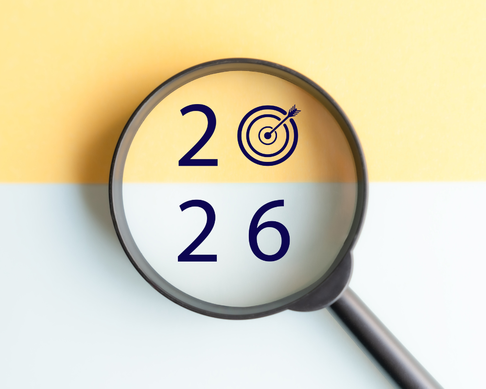A magnifying glass highlights the numbers "2026" with a target symbol replacing the zero, set against a yellow and white background—symbolizing the 2026 M&A Market outlook for business owners.